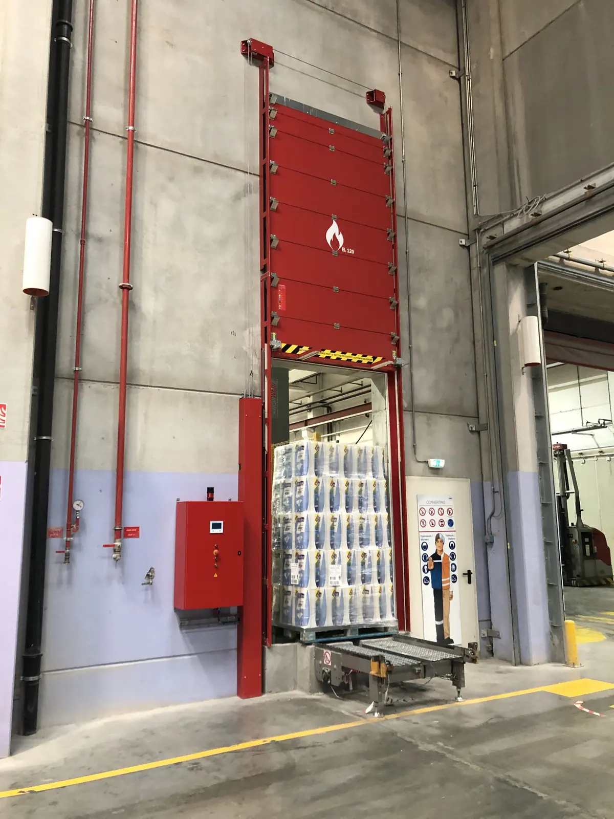 Porte coupe-feu à dévêtissement vertical relevée au-dessus d'un convoyeur